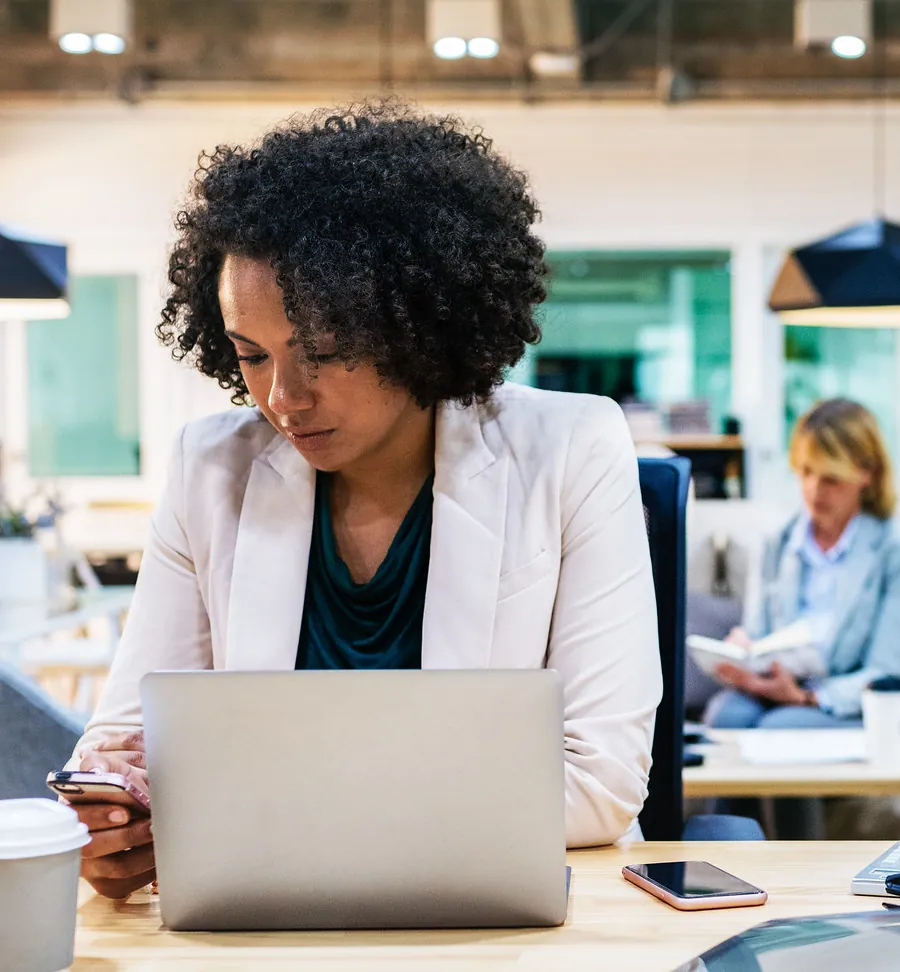 Une femme travaille sur son ordinateur, son téléphone à la main